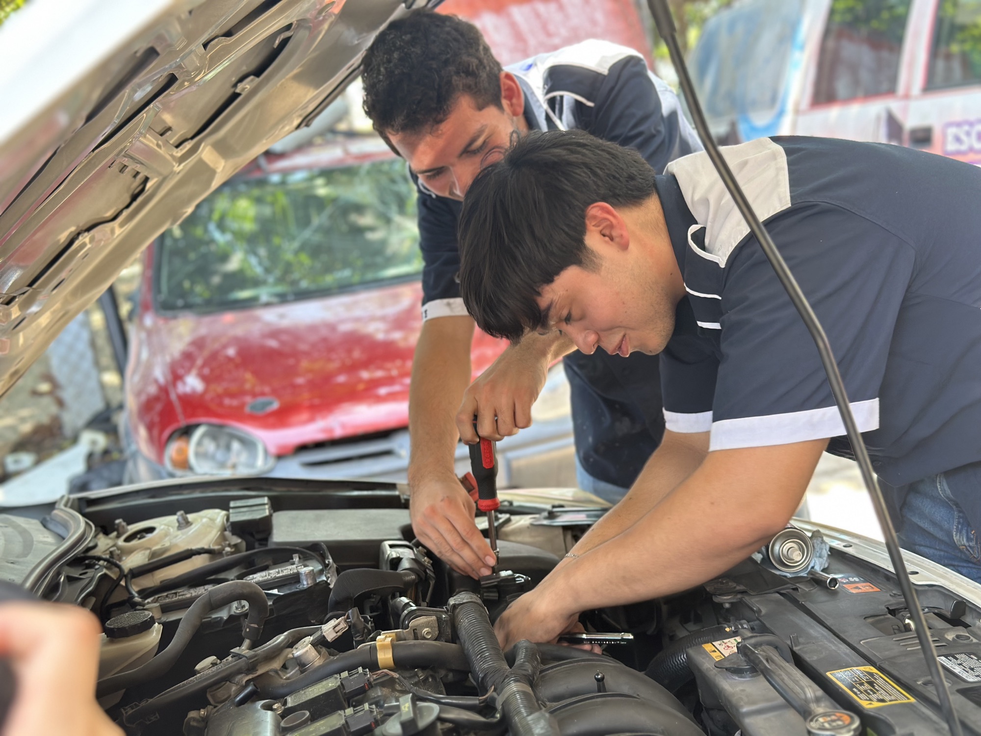 Estudiantes de Universidad ITE realizando una práctica bajo el cofre de un automóvil